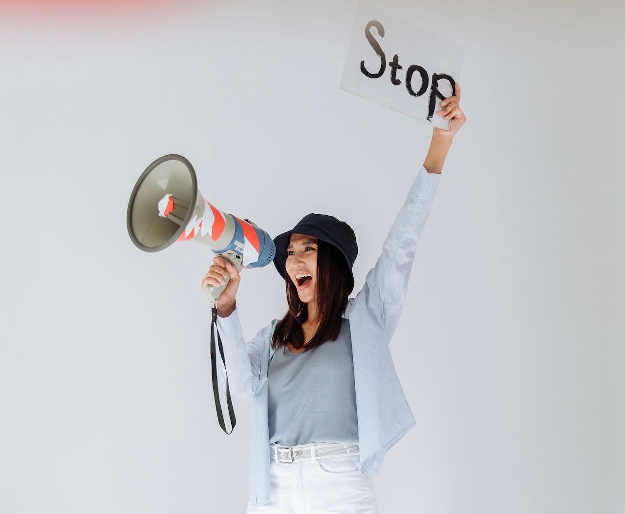 Eine Frau ruft in ein Megafon und hält ein Pappschild mit dem Wort „Stop“ hoch. 